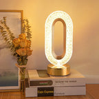 Abajur moderno oval iluminado sobre livros, ao lado de bouquet seco de rosas e quadro com decoração minimalista