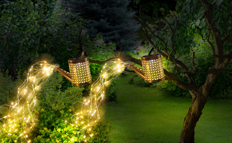 Regadores decorativos com luzes LED pendurados em galhos de árvore em jardim à noite