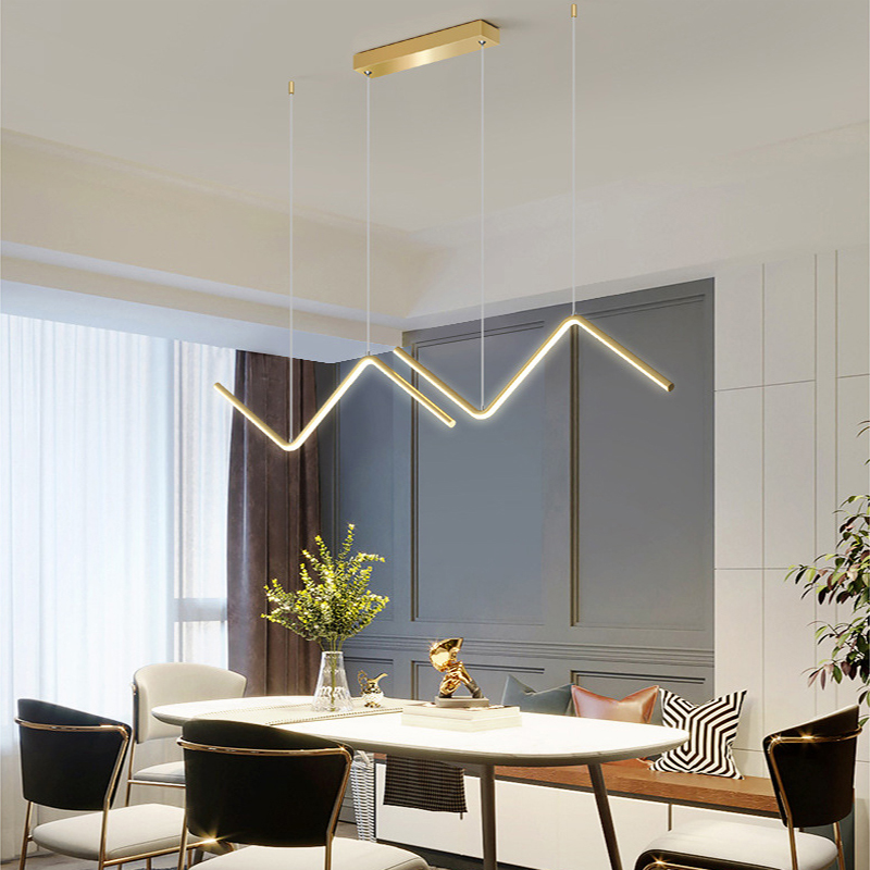 Luminária pendente dourada moderna em formato geométrico iluminando mesa de jantar com cadeiras em ambiente interno