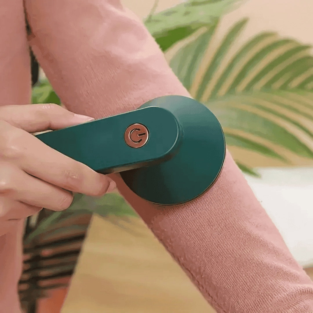 Pessoa usando removedor de pelos elétrico verde em manga de suéter rosa com planta ao fundo