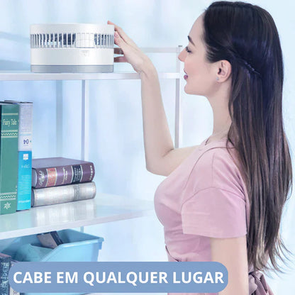 Mulher ajustando ventilador portátil branco em estante junto a livros em ambiente interno