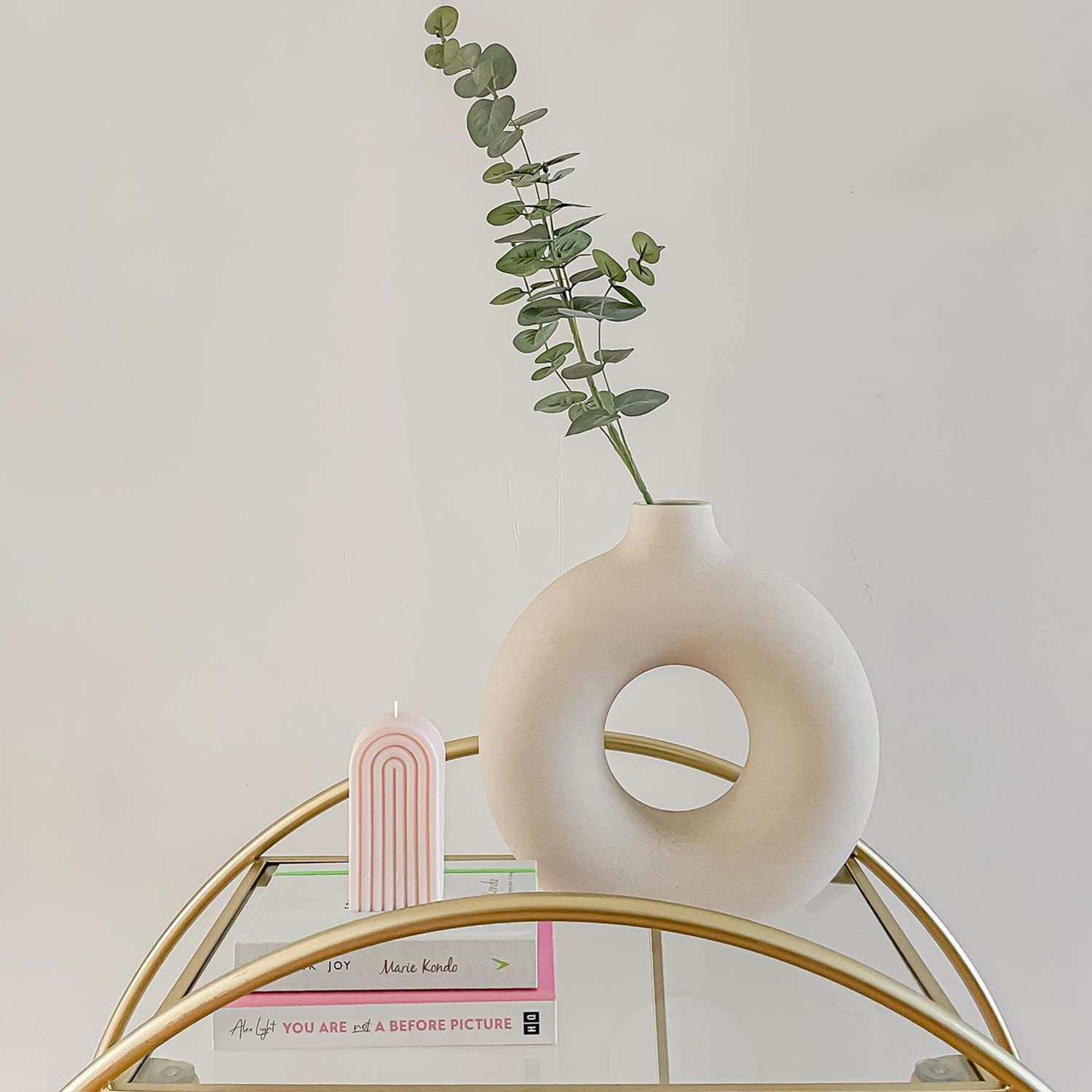 Vaso decorativo branco redondo com planta verde, vela rosa arco-íris e livros em mesa dourada