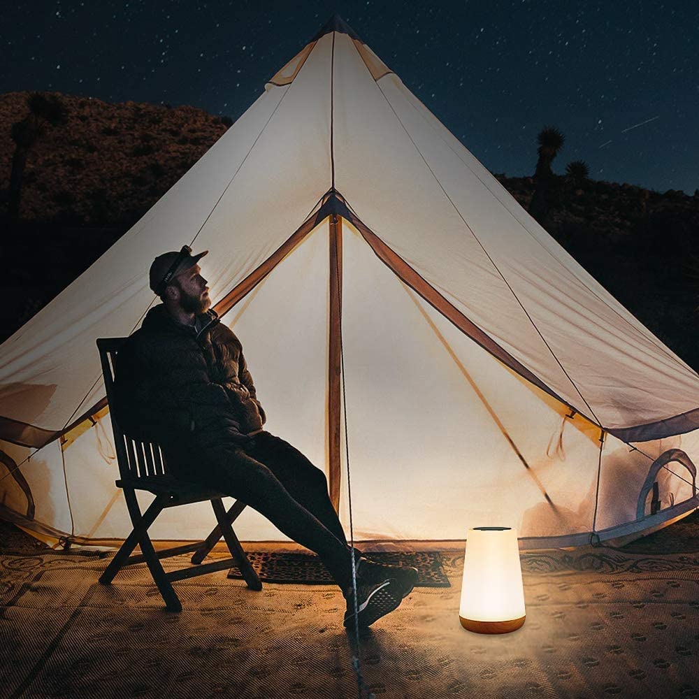 Homem sentado em cadeira de madeira à noite em frente a tenda iluminada, com luminária portátil acesa