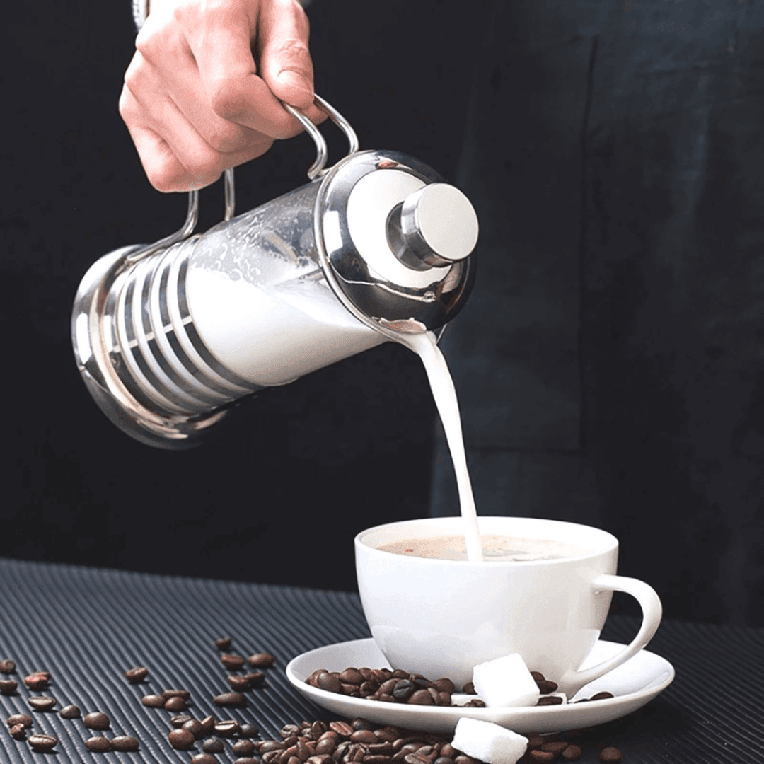 Mão servindo leite de prensa francesa em xícara branca de café com grãos e cubos de açúcar