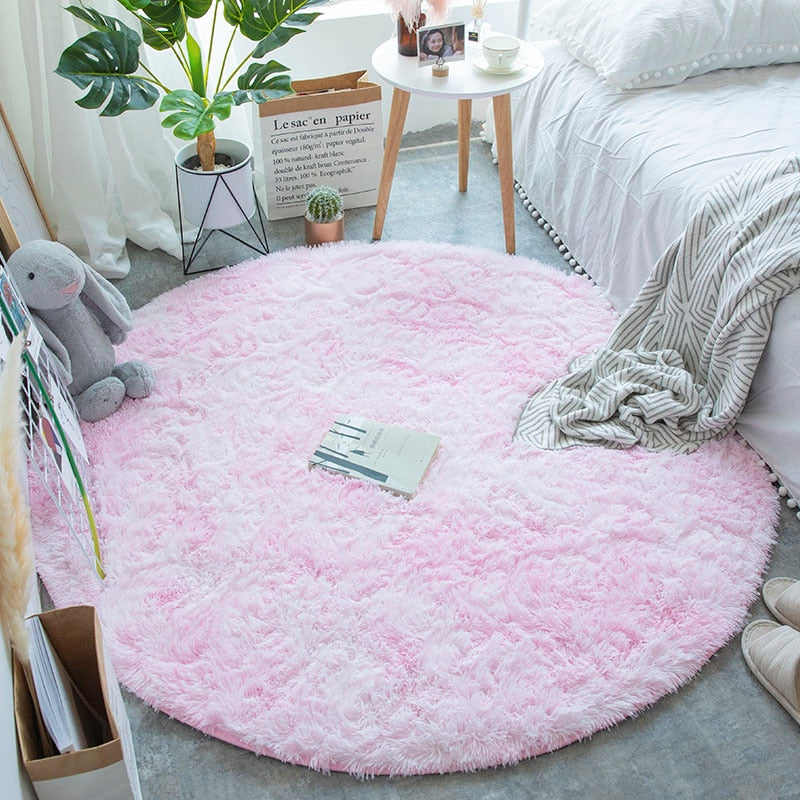 Tapete peludo redondo rosa claro em quarto aconchegante com cama branca, manta cinza, e planta decorativa
