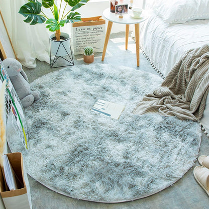Quarto aconchegante com tapete redondo felpudo cinza, planta, mesa lateral e roupa de cama branca