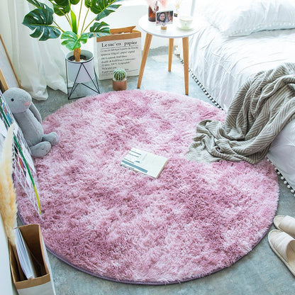 Tapete redondo rosa felpudo em quarto decorado com plantas, mesa lateral, cama branca e brinquedo de pelúcia cinza
