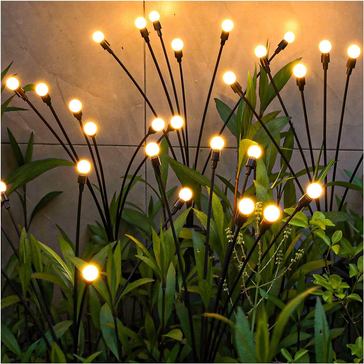 Luzes decorativas de jardim em hastes pretas entre plantas verdes com fundo de parede