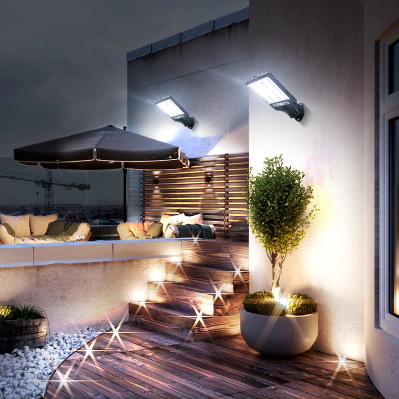 Refletores solares LED iluminando área externa com sofá, guarda-sol e escada de madeira à noite