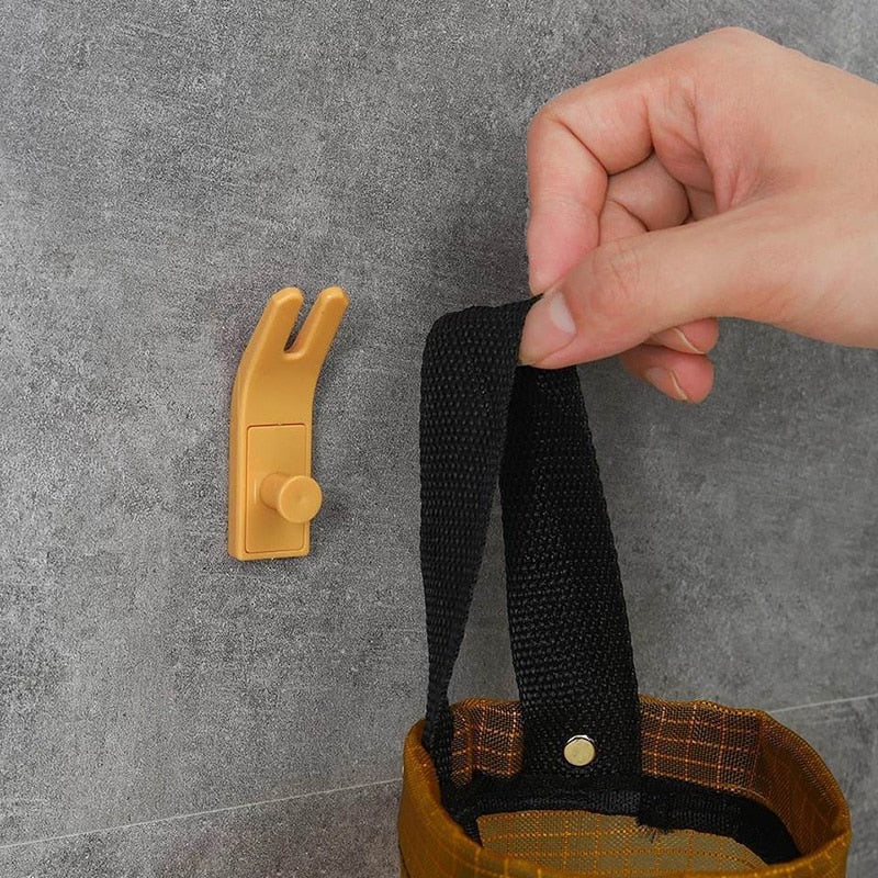 Mão pendurando alça preta de bolsa em gancho adesivo dourado em parede cinza
