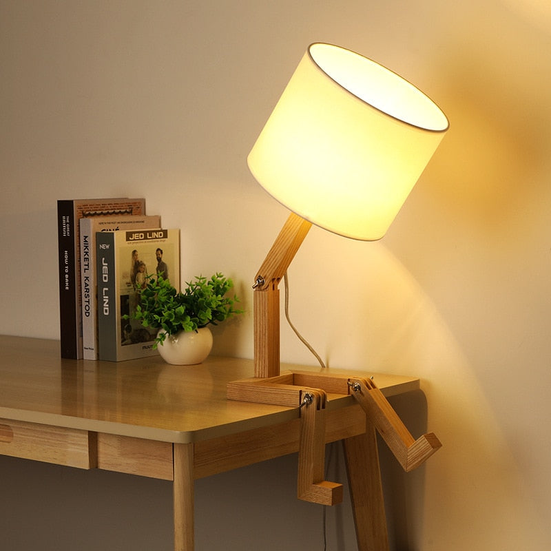 Abajur de madeira articulado com cúpula branca em mesa com livros e vaso decorativo