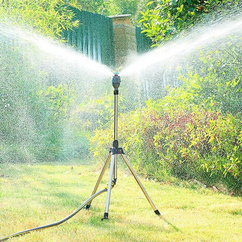 Aspersor de jardim em tripé irrigando grama e arbustos sob luz solar forte