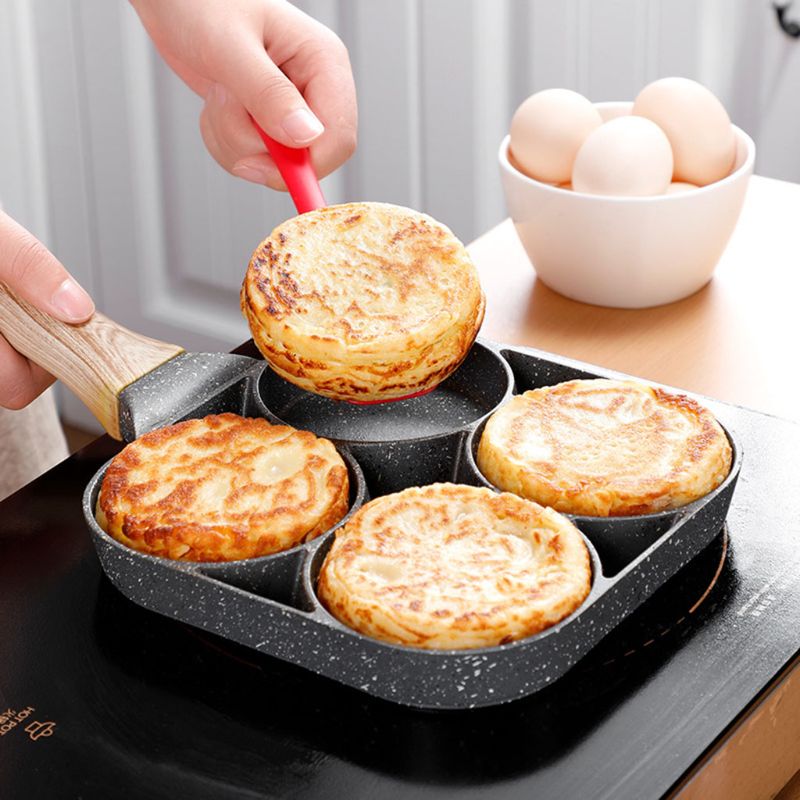Bolos dourados sendo preparados em frigideira antiaderente de 4 cavidades com alça de madeira em cooktop