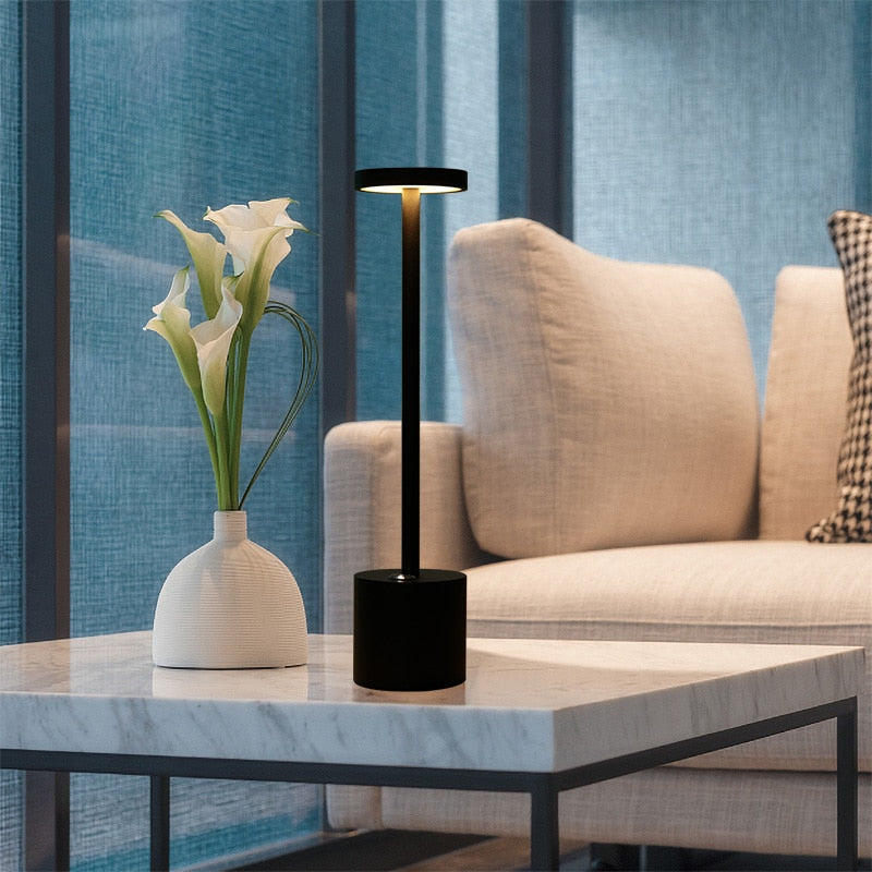 Abajur moderno preto e vaso branco com flores em mesa de mármore na sala com sofá bege