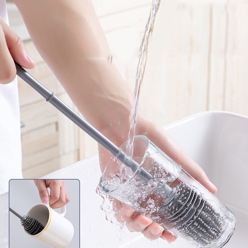 Escova de limpeza de copos de silicone cinza sendo lavada em água corrente em cozinha clara