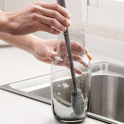 Mãos limpando jarra de vidro com escova de silicone cinza na pia da cozinha