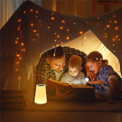 Pai e duas crianças lendo livro dentro de cabana iluminada com luzes de fada e lanterna