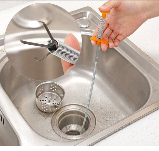 Mão segurando ferramenta de limpeza de ralos com gancho de metal em pia inox de cozinha