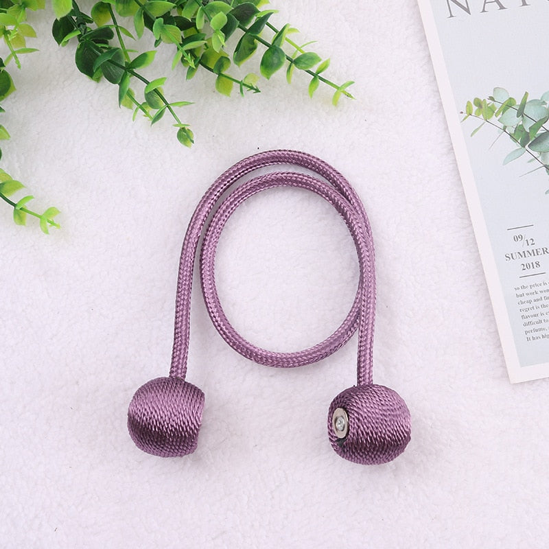Cordão roxo decorativo com extremidades arredondadas sobre fundo branco, plantas verdes e cartão de texto ao lado