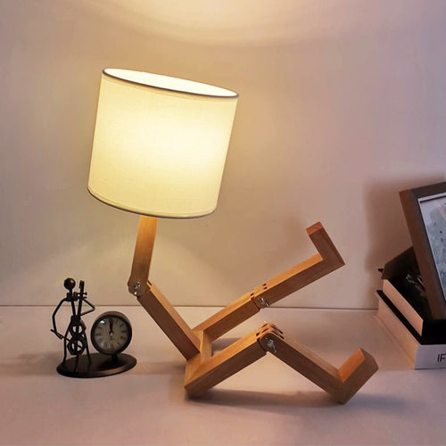 Abajur com design de madeira articulada em forma de pessoa sentado, luz quente, relógio e escultura ao fundo