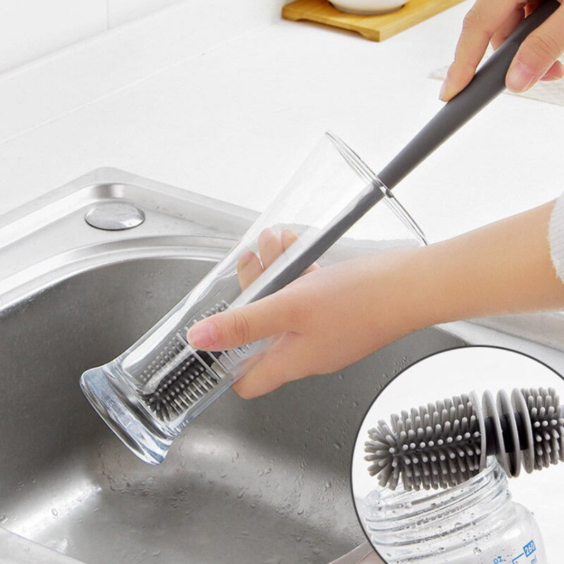 Pessoa lavando copo de vidro alto com escova de silicone cinza na pia de inox
