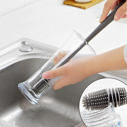 Pessoa lavando copo de vidro alto com escova de silicone cinza na pia de inox