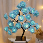 Árvore decorativa com flores azuis iluminadas em mesa redonda branca, fundo com cortina bege e luzes acolhedoras