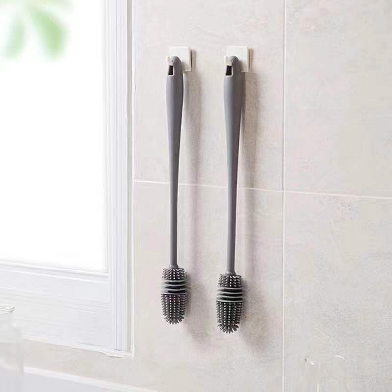 Escovas de silicone cinza penduradas em ganchos brancos na parede do banheiro