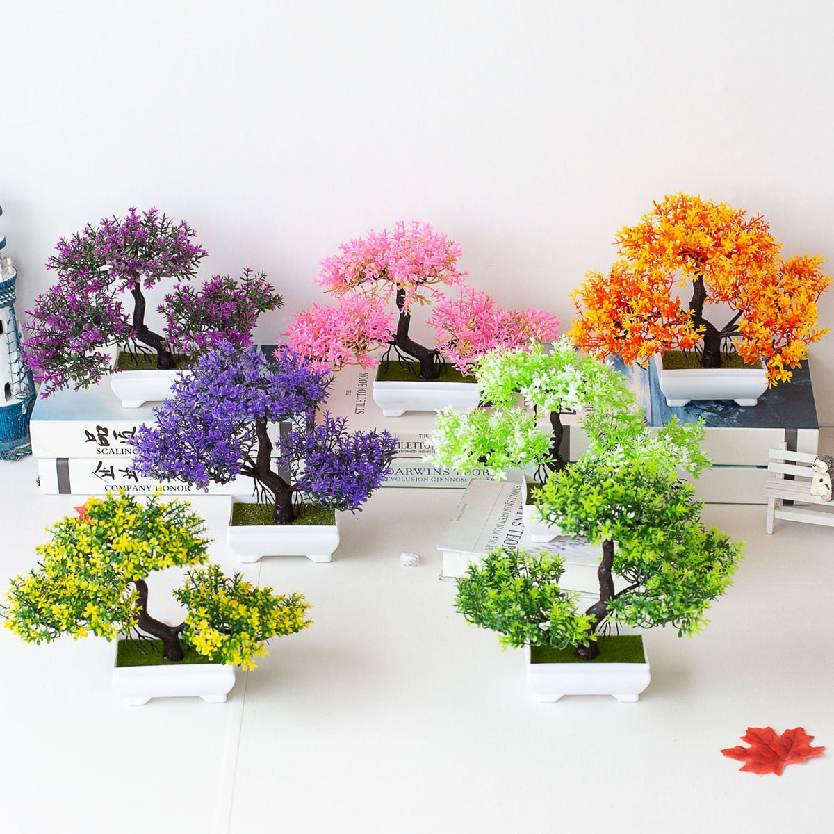Set de mini árvores decorativas com flores artificiais coloridas em vasos brancos sobre livros