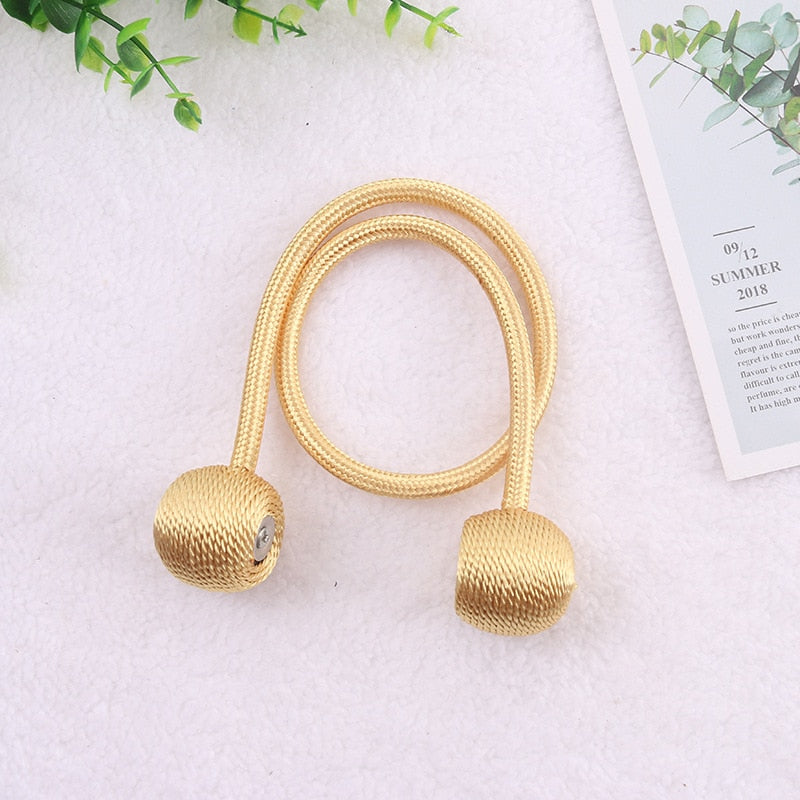 Cordão dourado decorativo para cortina com acabamentos em esfera sobre superfície branca