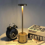 Relógio despertador preto, luminária dourada acesa em mesa branca com livros de design