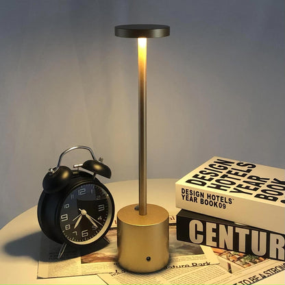 Relógio despertador preto, luminária dourada acesa em mesa branca com livros de design