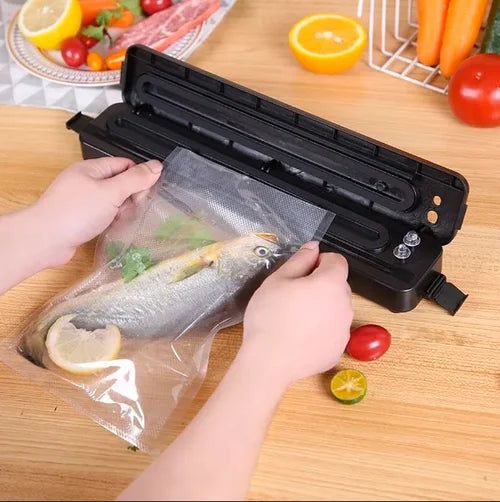 Seladora a vácuo preta embalando peixe com legumes frescos em cozinha
