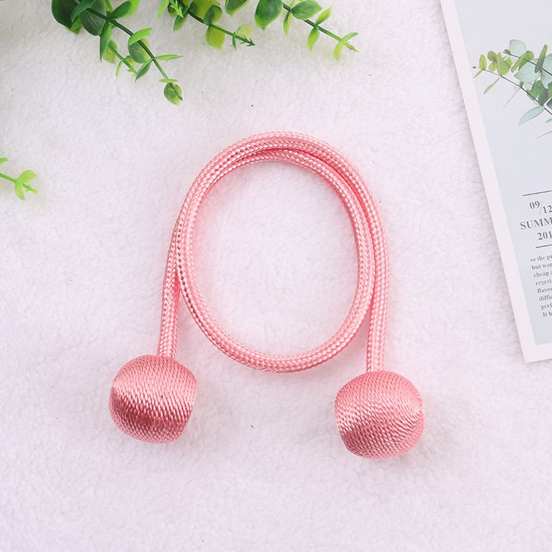 Cortina rosa com bolas de tecido decorativa em fundo branco com folhas verdes