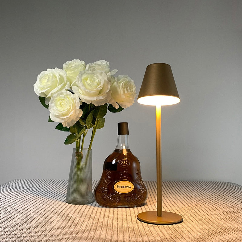 Vaso com rosas brancas, garrafa de Hennessy XO e luminária dourada sobre mesa texturizada