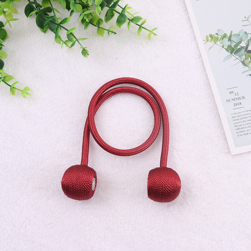 Cordão de cortina vermelho com pontas redondas sobre fundo branco com plantas verdes