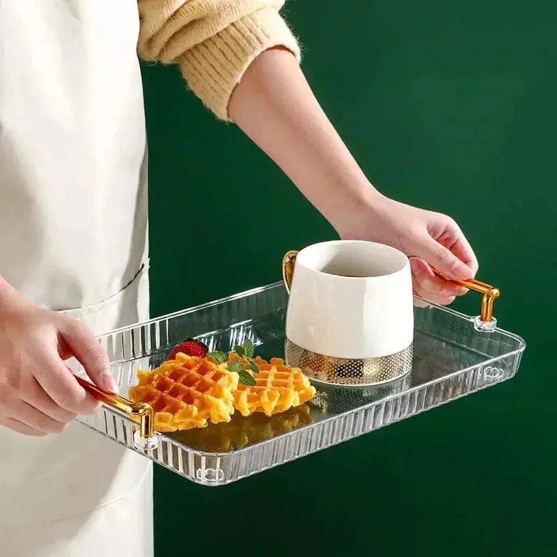 Bandeja transparente com alças douradas segurando duas waffles e uma xícara branca com detalhe dourado