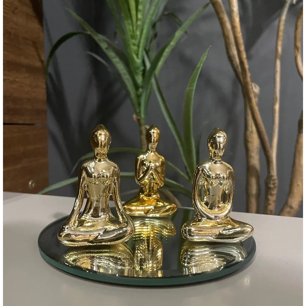 Trio de esculturas douradas de figuras femininas sentadas em posição de meditação sobre espelho