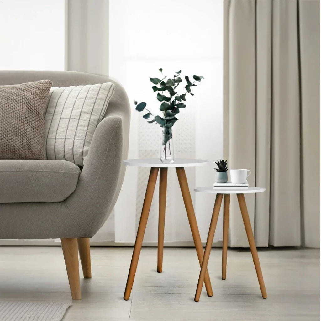 Mesa de centro nordica branca com pernas de madeira e vaso com folhagem ao lado de sofa cinza com almofadas