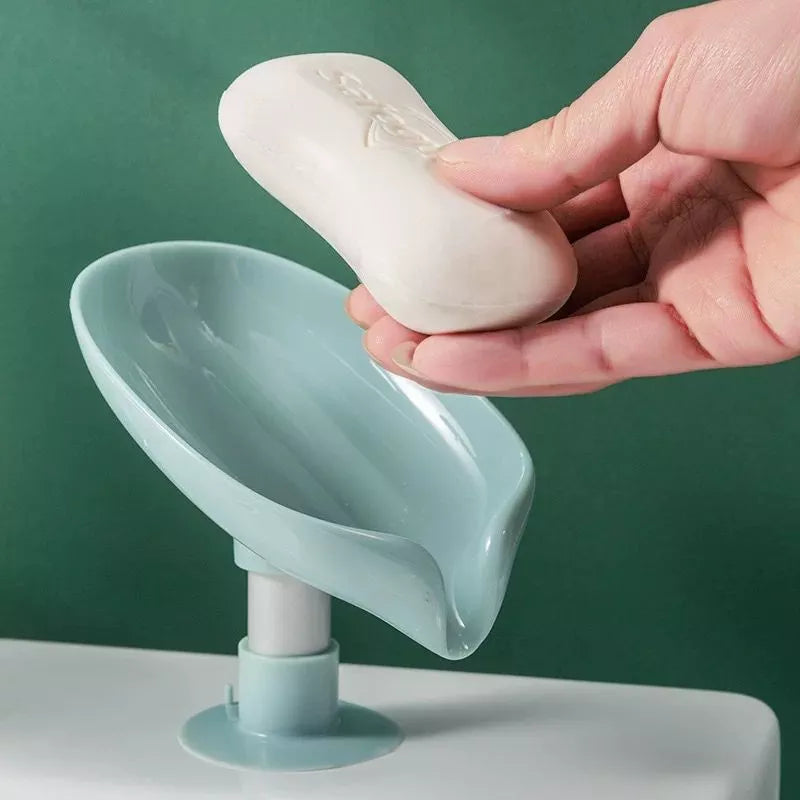 Saboneteira de plástico azul clara com sabonete branco sendo colocado à mão, fundo verde