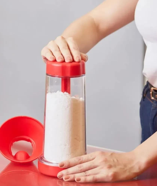 Moedor manual vermelho para farinha com tampa removida, mãos ajustando aparelho na cozinha