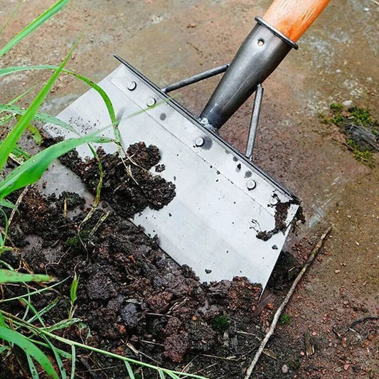 Enxada com cabo de madeira removendo terra úmida e grama em jardim