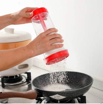 Mãos despejando sal de saleiro vermelho em frigideira preta no fogão de cozinha branca