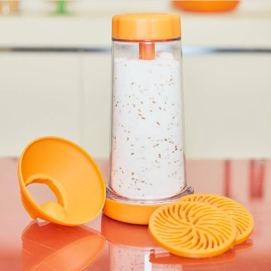 Purificador de ambiente com tampa e filtro laranja, com infusão branca e partículas visíveis, sobre mesa vermelha