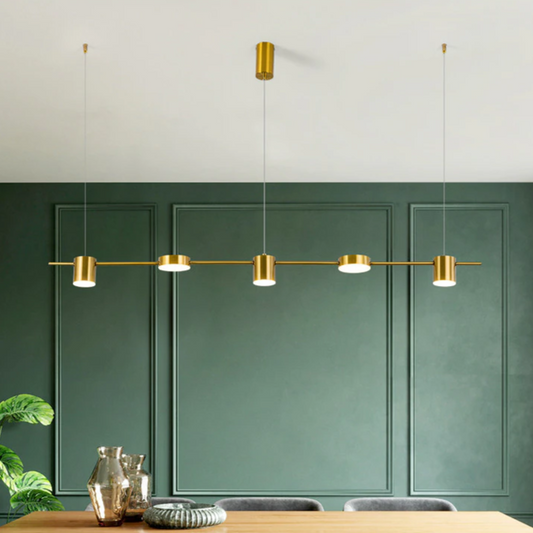 Luminária moderna dourada suspensa sobre mesa de madeira em sala com parede verde escura e decoração minimalista
