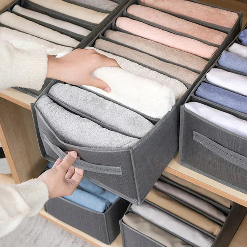 Organizador cinza para roupas com várias divisórias, armazenando toalhas e roupas dobradas em estante de madeira