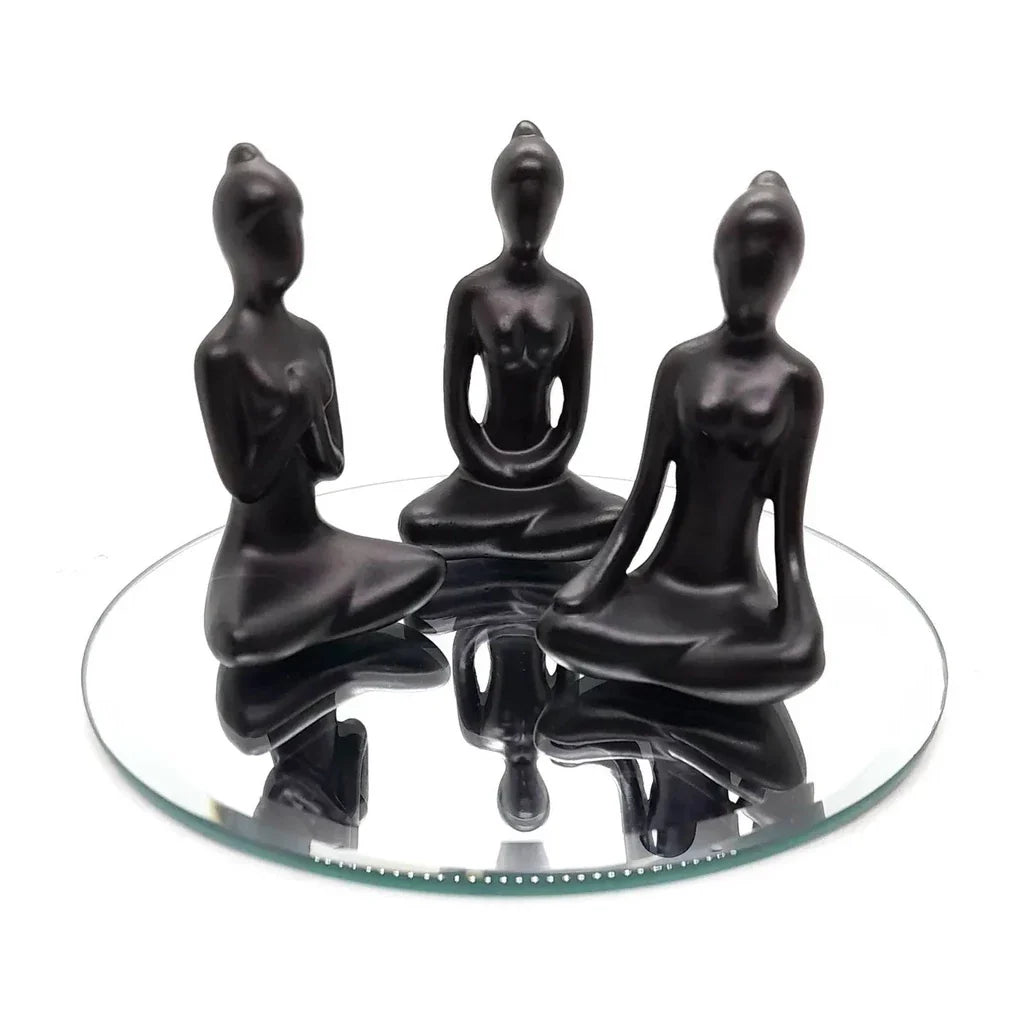 Trio de estátuas negras de yoga em posição sentada refletidas em espelho redondo