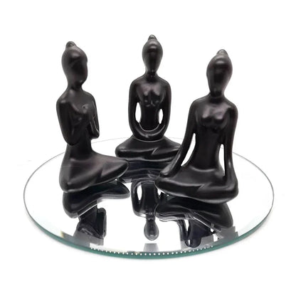 Trio de estátuas negras de yoga em posição sentada refletidas em espelho redondo