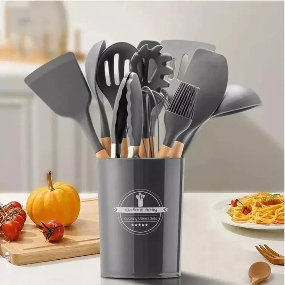 Conjunto de utensílios de cozinha em suporte cinza, com preparação de prato de macarrão e legumes ao fundo