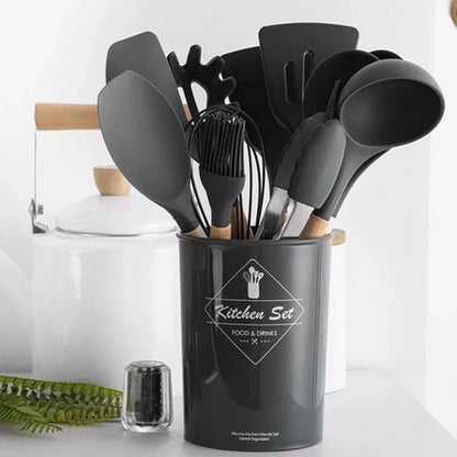 Conjunto de utensílios de cozinha pretos com cabos de madeira em suporte cinza, ao lado de panela branca